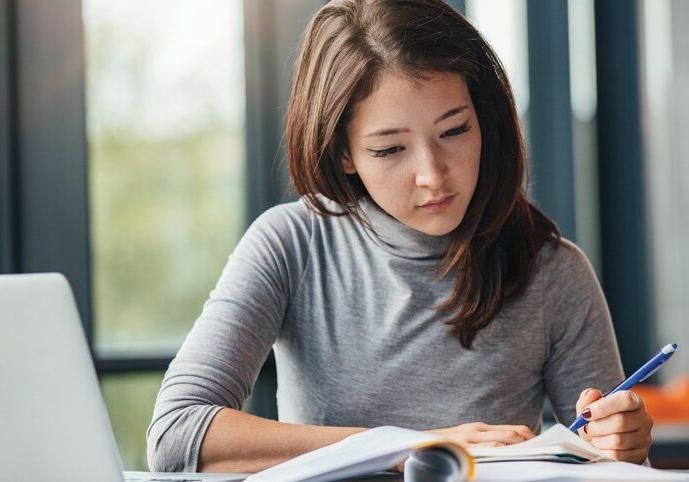 Shot of young woman taking down notes in diary. Female university student preparing note for the exam at library.